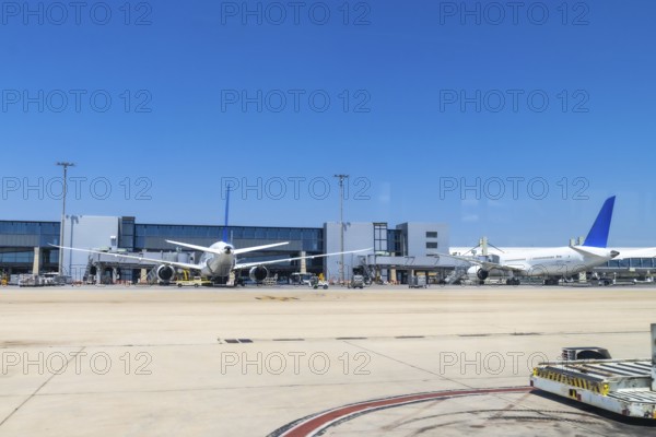Two large passenger airplanes parked at airport gates under a bright sunny sky, waiting for