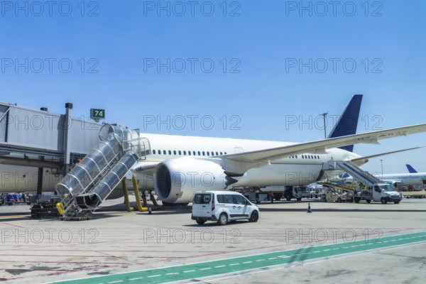 Modern passenger airplane parked at airport gate, connected to jet bridge, with ground crew and