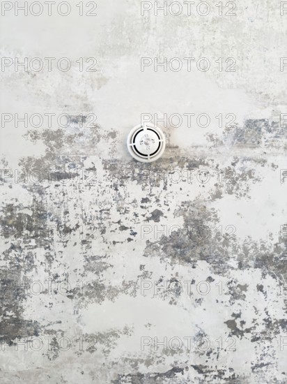Round ceiling sprinkler nozzle in minimalistic concrete ceiling with chipped paint and abstract