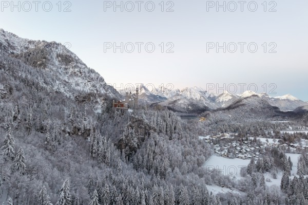 Neuschwanstein Castle in a wintry mountain landscape with snow-covered trees and mountains in the