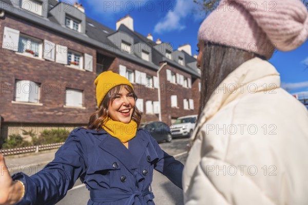 Two cheerful women friends dressed in winter clothes meeting and greeting each other with open arms