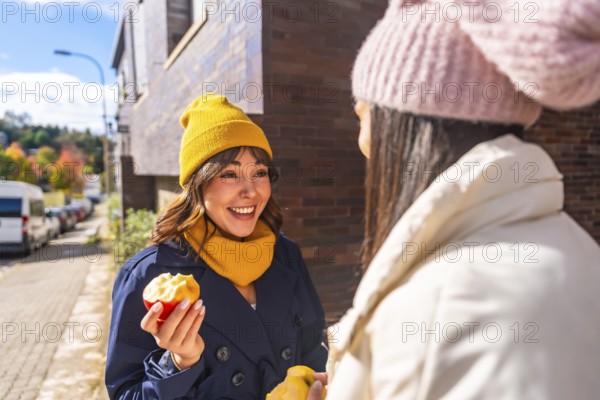 Two cheerful women friends enjoying fresh apples and engaging in a conversation outdoors on an