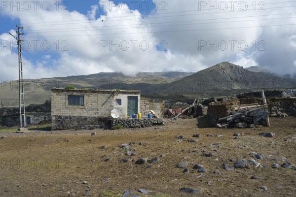 A simple stone house with power lines in a mountainous landscape, village at the foot of Great
