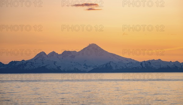 View of Cook Inlet on white mountain peaks of Mount Iliamna at sunset, picturesque golden light of