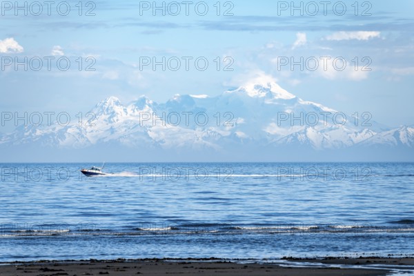 View over Cook Inlet to white mountain peaks of Mount Iliamna, motor boat rides on the ocean,