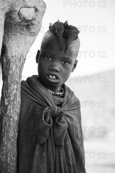 Black and white, Himba girl leaning at a traditional clay hut, in the morning, traditional Himba