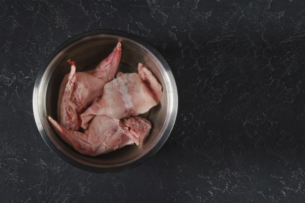 Fresh rabbit hind legs and a saddle are soaked in water with vinegar in a metal bowl. The process