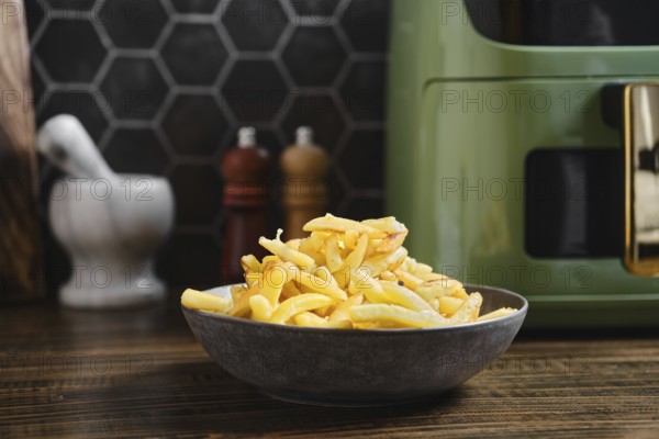 Fries are piled high in a dark bowl on a kitchen counter. The setting features a stylish air fryer