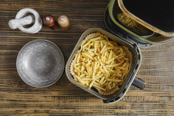Golden fries are freshly cooked in an air fryer, resting in a basket lined with paper. A ceramic