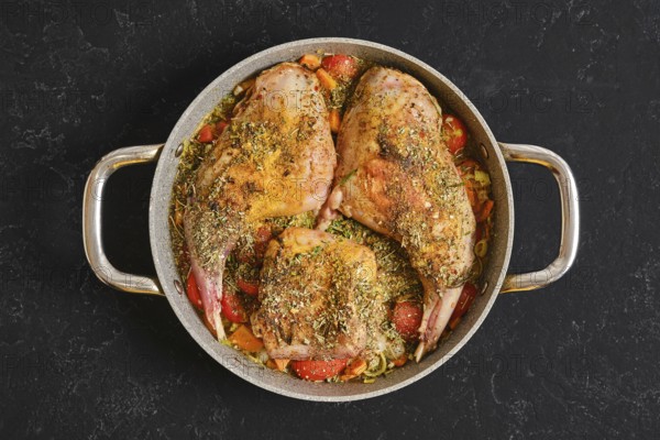 Two rabbit hind legs and a saddle are seasoned with herbs and spices, placed on a bed of colorful