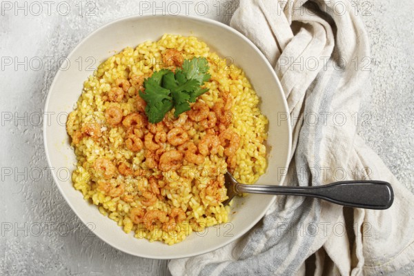 Risotto with shrimp, in a bowl, on a textured surface, with a side dish of fresh coriander,