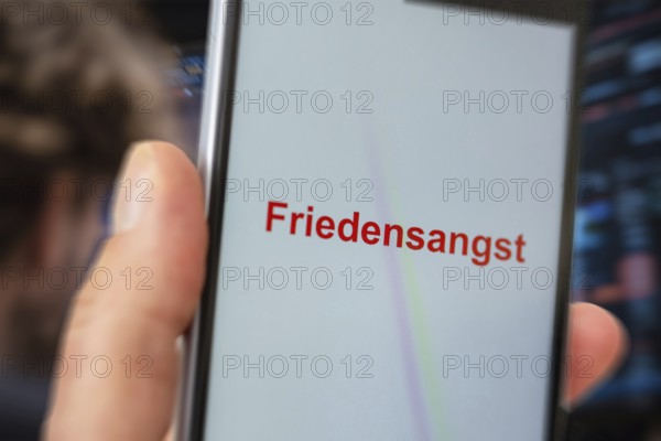 (photo montage) Smartphone with displayed text FEAR OF PEACE against the backdrop of a stock