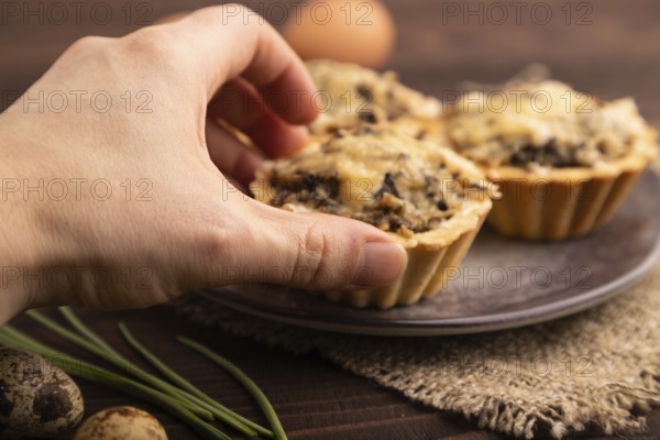 Tartlets with meat and cheese with hand on brown wooden background and linen textile. side view,