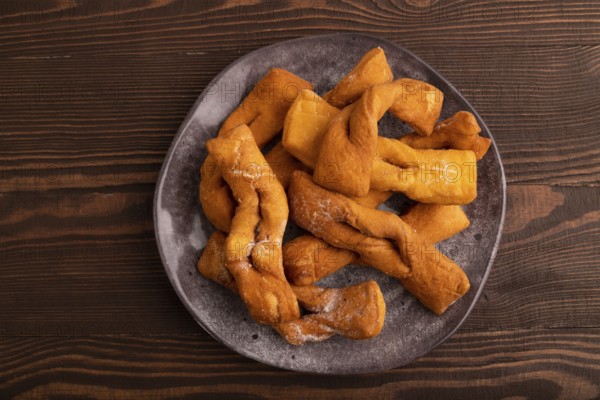 Crunchy biscuit Brushwood cookies sprinkled with powdered sugar on brown wooden background, top