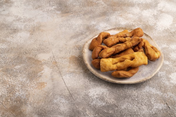 Crunchy biscuit Brushwood cookies sprinkled with powdered sugar on brown concrete background, side