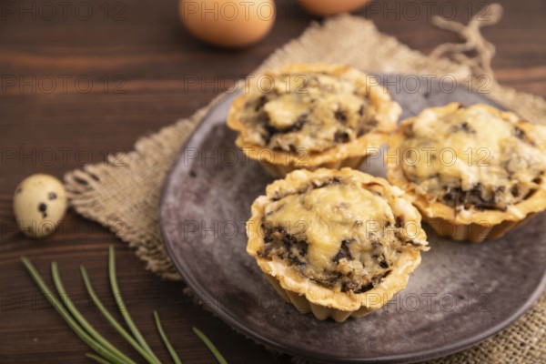Tartlets with meat and cheese on brown wooden background and linen textile. side view, close up,