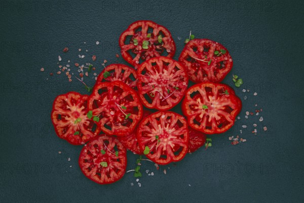 Freshly sliced ripe tomatoes arranged on a textured dark surface with herbs and salt scattered
