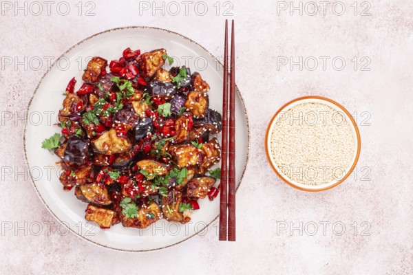 Fried eggplant, Chinese style, in sweet and sour sauce, with pepper and sesame seeds. on a white