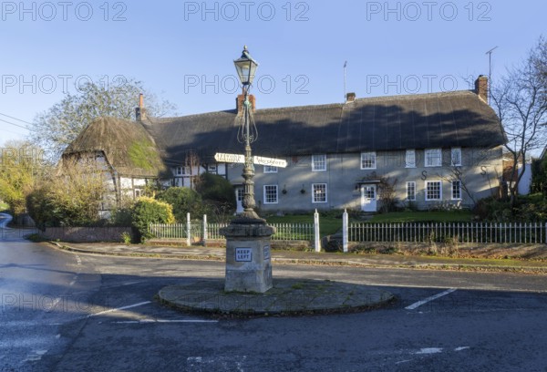 Historic signpost with direction arrows, thatched cottages in village of Pewsey, Wiltshire,
