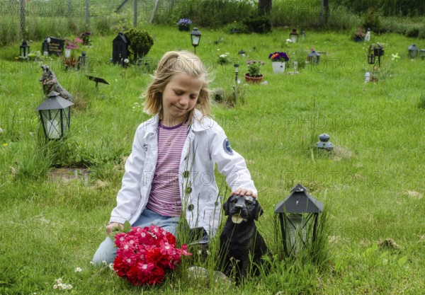 Grieving blonde 7-year-old girl at her dog's grave at pet cemetery in Ystad, Skåne County, Sweden,