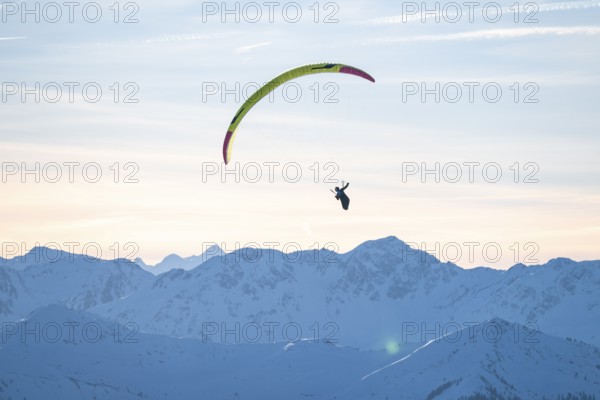 Paragliders flying over snowy mountain peaks in winter in evening light, Kitzbühel Alps, Tyrol,