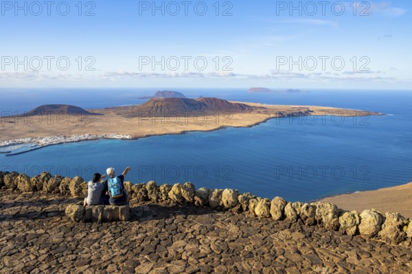 Tourists on a bench on the viewing platform at the Mirador del Río viewpoint, in the evening light,