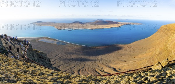 View of La Graciosa island with volcanic craters in the evening light, tourists on an observation