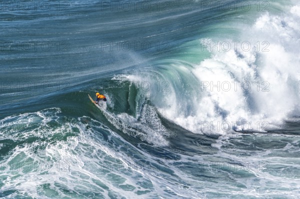 Surfers with their jet ski pilots in the Atlantic waves below Farol de Nazaré, Forte São Miguel,