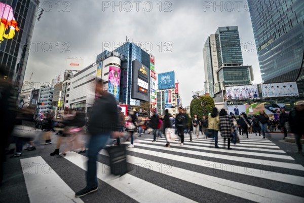 Crowd crossing zebra crossing on a large intersection, motion blur, back modern houses with