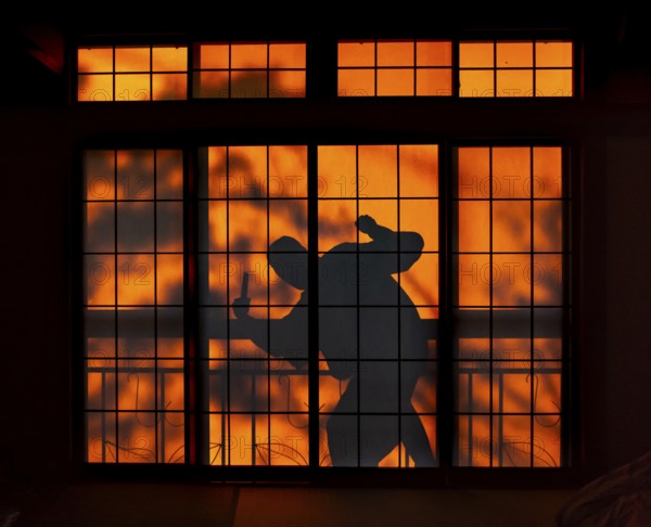 Shadow of a man, burglar with knife, assassin, ninja, on the balcony behind sliding shoji doors in
