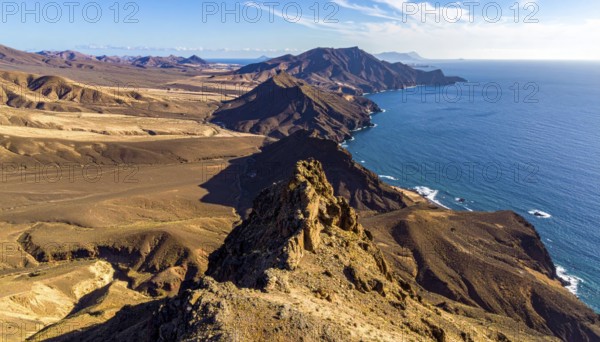 Desert landscape converges with ocean along a rugged coastal area, shore break at cliffs, blue