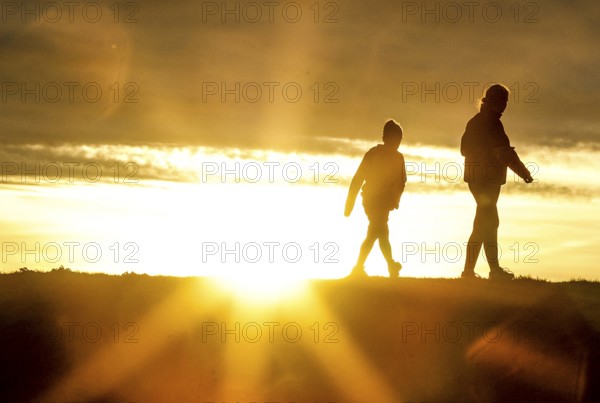 Woman and child walk across a dike on the island of Fehmarn at sunset, 13.10.2025, Fehmarn,