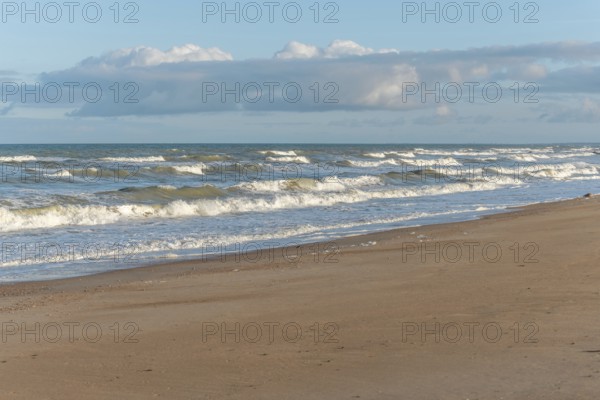 The waves crash gently against a rocky shoreline at sunset, creating a tranquil atmosphere. The