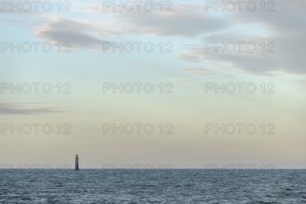 A lighthouse rises from the gentle waves of the ocean, surrounded by a tranquil seascape. Soft
