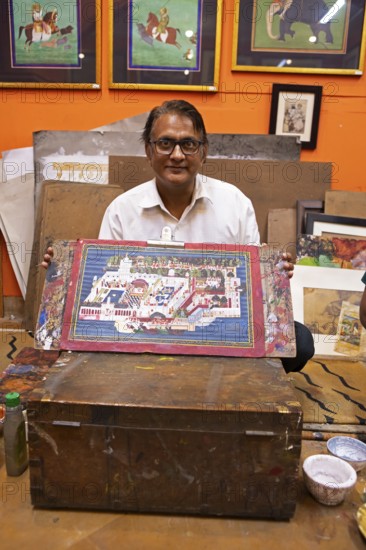 Miniature painter, 50 years old, shows a picture of the royal city palace in his studio, Udaipur,