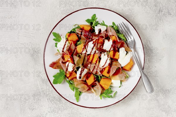 Salad with slices of ripe melon, prosciutto, mozzarella and fresh arugula, decorated with balsamic