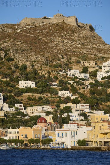 Panteli Fortress, White houses stretch along a hill with a fortress at the top and the sea in the