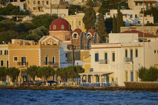 Colourful coastal houses with church and trees by the water, sunny city panorama, Agia Marina,