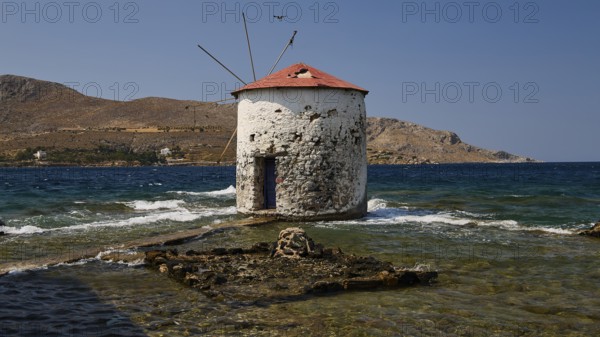 Old windmill in the middle of the sea, surrounded by foaming waves and a deep blue sky, Agia