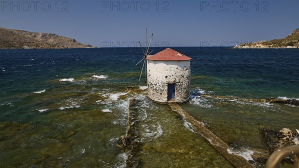Historic windmill stands in the turquoise sea, surrounded by waves and a clear sky, Agia Marina,