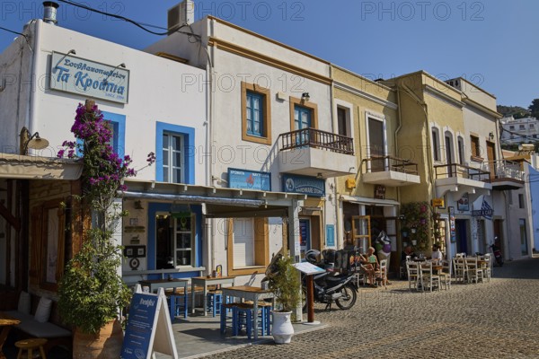 Row of historic buildings with restaurants and flowers on cobblestone street in sunshine, Agia