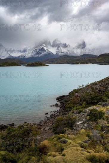 Cloudy mountain range Cuernos del Paine, shore of the blue lake Lago Pehoe in the evening light,
