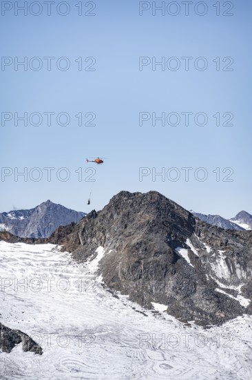 Helicopter with a load on a rope flies over glaciers and mountains, Stubai Alps, South Tyrol, Italy