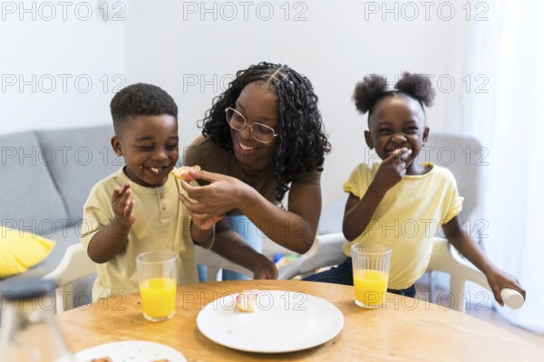 Mother joyfully feeding her children during a cozy breakfast at home, creating a warm atmosphere