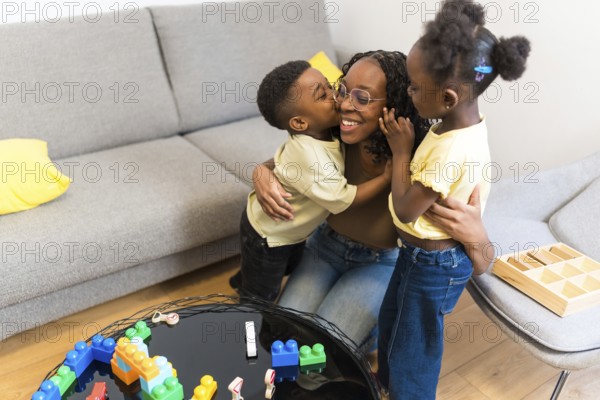 Cheerful mother enjoying time with her two loving children, embracing and kissing in the living