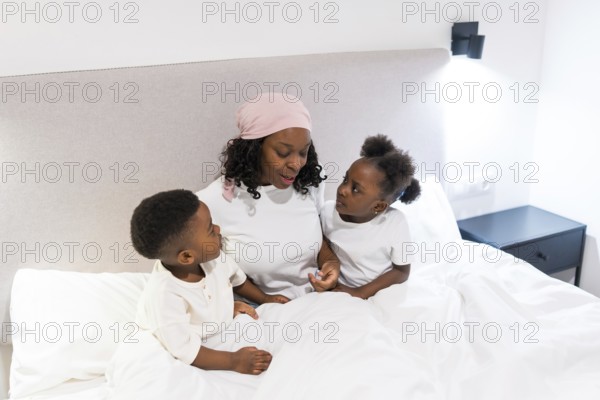 Mother undergoing cancer treatment, wearing a headscarf, sharing a heartwarming moment with her two