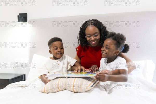 Smiling mother sharing a bedtime story with her two joyful children while cozily nestled on the
