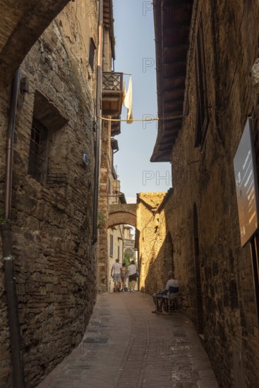 Alley in San Gimignano with historic walls, laundry in the wind and an elderly man on a chair, San