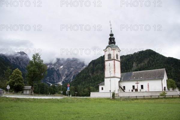 White church building against a mountainous background under a cloudy sky, Zgornje Jezersko,
