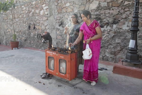 Indian woman lighting tea lights at a fire hydrant, Govind Dev Ji Hindu temple in the old city